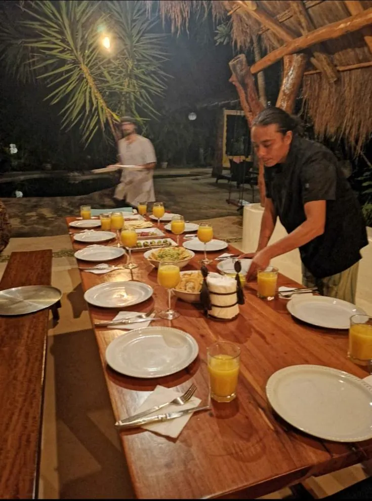 A long villa table being set under palapa light at night